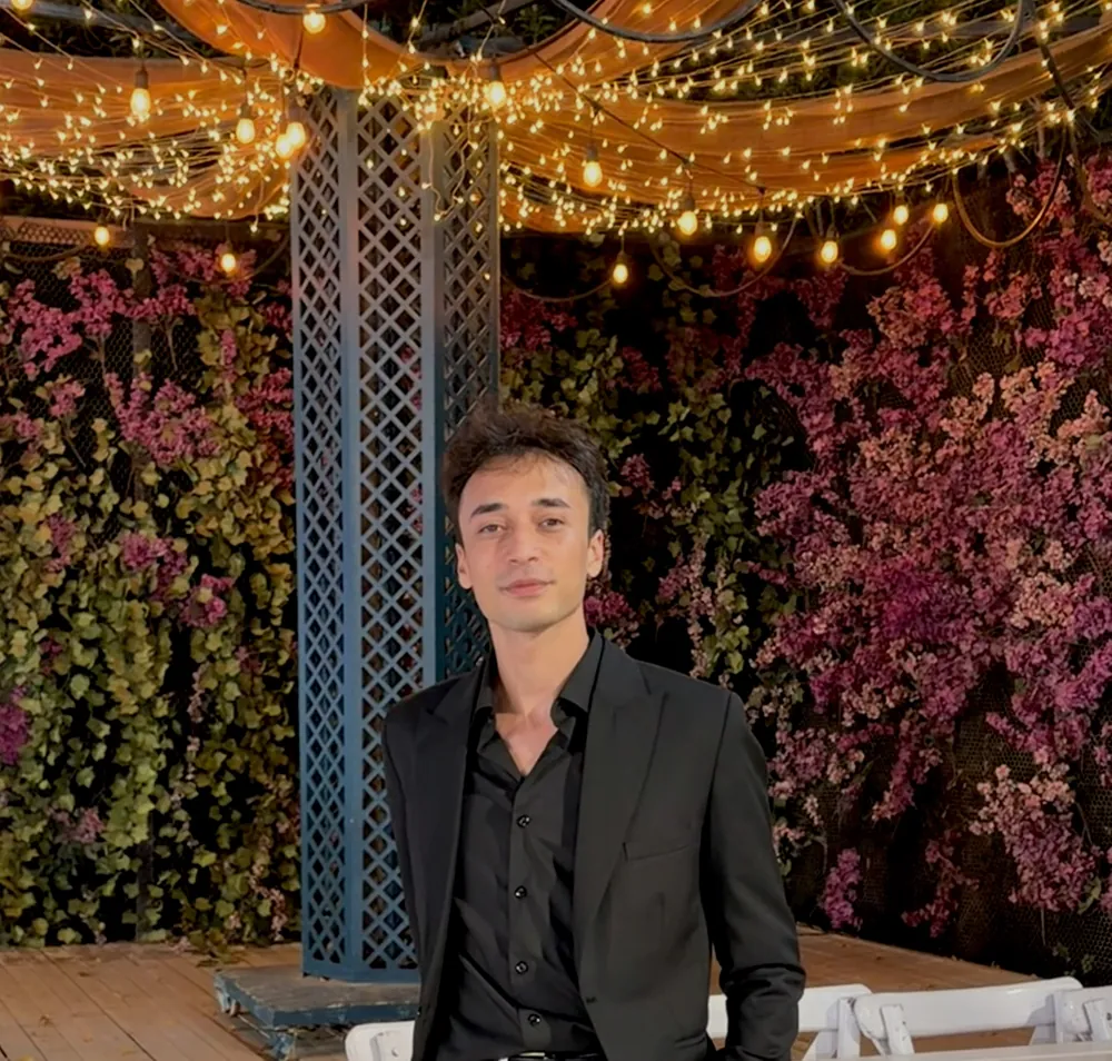 Ahmed in a black suit under string lights